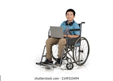 Preteen Boy Student Sitting In A Wheelchair While Using A Laptop In The Studio, Isolated On White Background