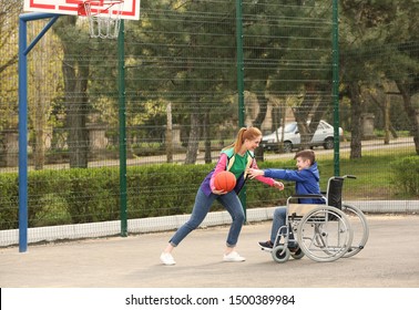 Preteen boy in wheelchair and young woman playing basketball on sports ground