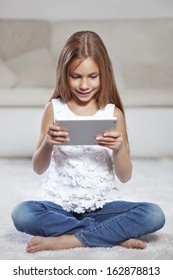 Preteen Child Playing On Ipad Sitting On A Carpet At Home