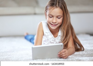 Pre-teen child playing on ipad tablet pc resting on a carpet at home