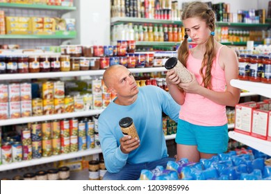 Preteen girl with father choosing different goods in grocery shop
