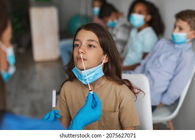 Preteen Girl Getting Tested For Coronavirus Sitting With Multiethnic Group Of Children In Clinic Indoors. Nurse Making PCR Test For Kids. Coronavirus Diagnostic Concept. Selective Focus
