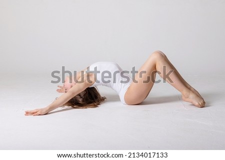 preteen girl gymnast trains on white background in white leotard. children's professional sports, rhythmic gymnastics
