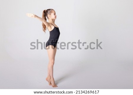 preteen girl gymnast trains on white background in black leotard. children's professional sports, rhythmic gymnastics