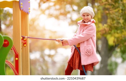 Preteen Girl Kid Climbing On Playground At Autumn Park And Smiling. Happy Female Child Portrait Outdoors