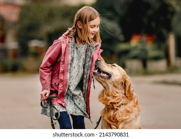 Preteen girl in pink jacket with golden retriever dog smiling at street. Pretty child kid with pet doggy labrador spend time outdoors