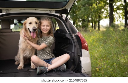 Preteen Girl Sitting With Golden Retriever Dog In The Car Trunk And Smiling Looking At The Camera. Child Kid Hugging Purebred Doggy Pet In The Vehicle At The Nature