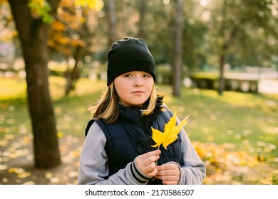 Preteen Girl Walking At Autumn Park And Holding Maple Leaf.