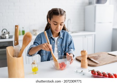 Preteen Kid Mixing Cherry Tomatoes In Bowl Near Cutting Board And Olive Oil In Kitchen