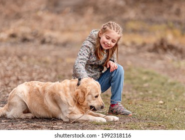 Preteen little girl smiling and petting golden retriever dog while it eats stick