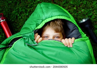 Preteen School Kid Boy In Sleeping Bag Camping. Outdoors Activity With Children In Summer. Fun And Adventure Camp, Family And Friends Vacations Or Weekend Trip. Portrait Of Child With Flashlight.