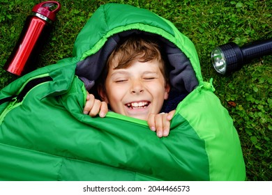 Preteen School Kid Boy In Sleeping Bag Camping. Outdoors Activity With Children In Summer. Fun And Adventure Camp, Family And Friends Vacations Or Weekend Trip. Portrait Of Child With Flashlight.