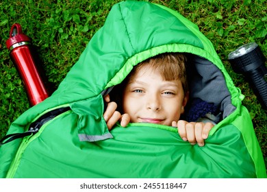 Preteen school kid boy in sleeping bag camping. Outdoors activity with children in summer. Fun and adventure camp, family and friends vacations or weekend trip. Portrait of child with flashlight. - Powered by Shutterstock