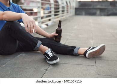 Pretending To Be Cool. Teen Guy Smoking Cigarette And Drinking Beer, Sitting On Roof Alone, Empty Space