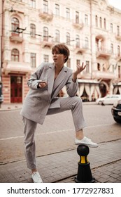 Pretentious Woman In Oversized Grey Suit Posing Outdoors. Full-lenght Portrait Of Short-haired Girl In Stylish Jacket And Pants Walking Outside