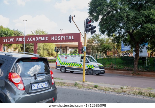 Pretoria, Gauteng, South Africa, April\
24 2020, steve biko academic hospital from across the road with\
traffic light and ambulance driving out of focus and\
grain