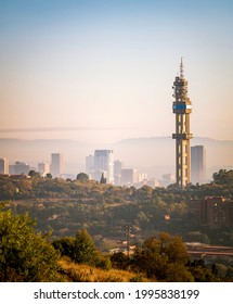 Pretoria, Gauteng, South Africa - June 22 2021:  The Telkom Communication Tower In Pretoria, Early On A Winter's Morning, During The Golden Hour.  Downtown Visible Through The Mist In The Background.