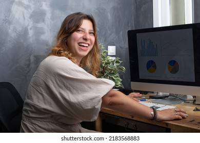 Pretty 25 Year Old Young Woman Working At Home On A Computer. She Is Laughing.
