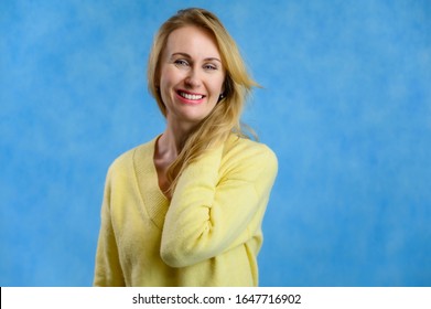 Pretty 40 Year Old Blond Woman In A Yellow Sweater Shows A Joyful Lifestyle On A Blue Background