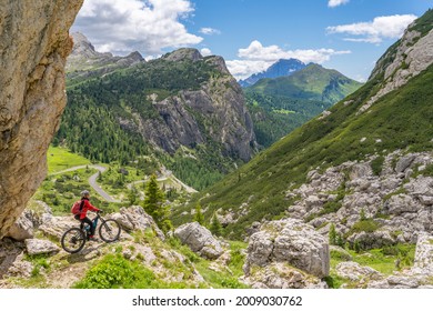 pretty active senior woman riding her electric mountain bike up to Valparola Pass  with awesome view down to Passo Falzarego in the Alta Badia Dolomites , South Tirol and Trentino, Italy