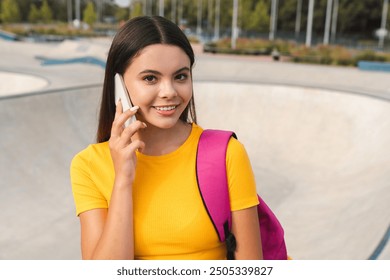 Pretty active young teen girl female skater sportswoman in casual with bag standing against ramp in city skate green park talking on mobile cell smart phone spending free time after school lessons - Powered by Shutterstock