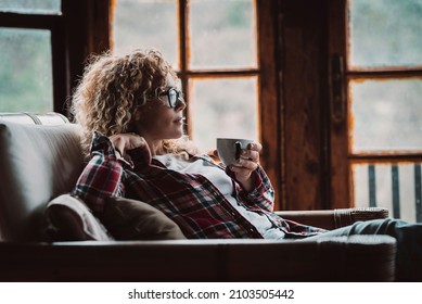 Pretty adult hipster woman sitting and relaxing at home with cup of tea and windows in background - relaxed and enjoyed female people in cozy cabin house for holiday vacation or alternative lifestyle - Powered by Shutterstock