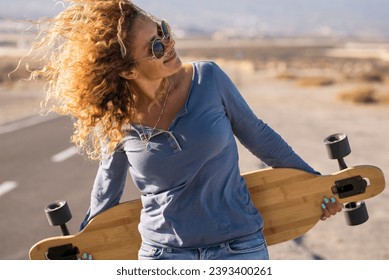 Pretty adult woman enjoy life and free lifestyle walking on a long asphalt road and holding long  board skate. Concept of happy beautiful female modern portrait in outdoor leisure activity. Active - Powered by Shutterstock