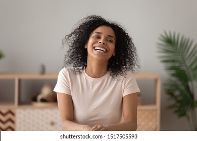 Pretty African American 30s Woman Sit At Table Indoors In Cozy Living Room At Home, Overjoyed Female Laughing Feels Happy Having Wide Toothy Smile Vlogger Recording New Video Vlog Looking Away Concept