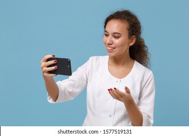 Pretty African American Doctor Woman Isolated On Blue Background. Doctor In Medical Gown Doing Selfie Shot On Mobile Phone Making Video Call. Healthcare Personnel Medicine Concept. Mock Up Copy Space