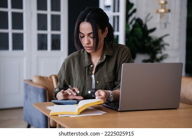Pretty African American pretty student girl sitting at desk with laptop, diary uses calculator counts profit of her business. Remote working Brazilian young woman tired, feels fatigue.