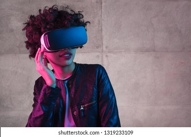 Pretty African American teenager in modern VR headset looking away while standing near concrete wall