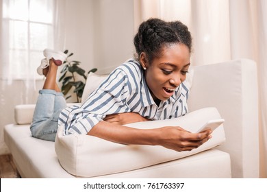 Pretty African American Woman Laying On Couch And Using Smartphone At Home