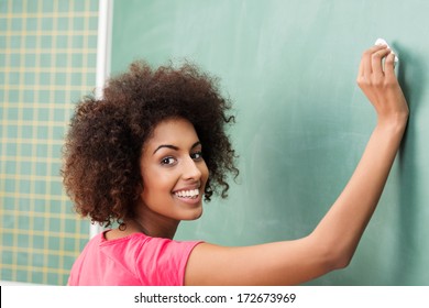 Pretty African American woman teacher in class writing on the blackboard as she teaches her students and turning to smile at the camera - Powered by Shutterstock