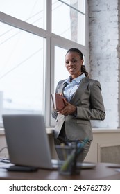 Pretty african business woman standing near window leaning windowsill at her office and taking notes in her diary while planning her day - Shutterstock ID 246762739