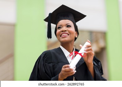 Pretty African College Student In Graduation Cap And Gown In Front Of School Building