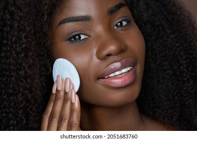 Pretty African ethnic black young woman holding cotton pad removing face make up with makeup remover cleanser on brown background. Oily skin care treatment, cleaning skincare routine concept.