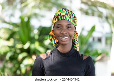 Pretty African Teenage Girl Wearing A Traditional Colorful Headscarf, Looking Directly Into The Camera With A Broad Smile; Concept Of Carefree Youth And Natural Freshness