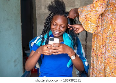 Pretty African Woman At A Home Made Salon For Hair Styling And Looking At Her Phone Smiling