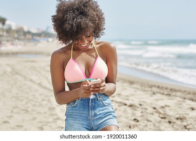 Hübsche Afro-Amerikanerin mit Handy am Strand lacht
