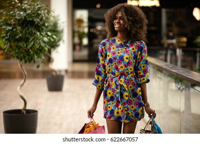 Pretty afro-american girl with curly hair and beautifll dress walking in a shopping mall.