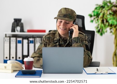 Pretty American soldier behind her computer talking on the phone in the office