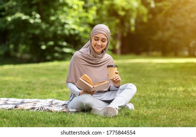 Pretty Arab Girl Reading Book And Drinking Coffee Or Tea At Park, Sitting On Grass