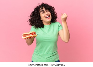pretty arab woman feeling shocked,laughing and celebrating success and holding a hot dog