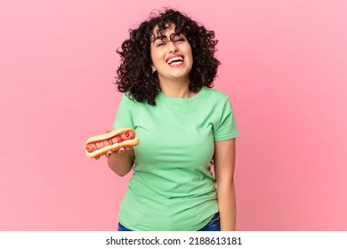 pretty arab woman looking happy and pleasantly surprised and holding a hot dog
