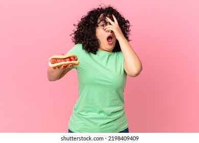 Pretty Arab Woman Looking Shocked, Scared Or Terrified, Covering Face With Hand And Holding A Hot Dog