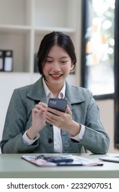 Pretty Asian business woman in black suit working at her office desk, with document file and paperwork. texting mobile smartphone or chat message - Shutterstock ID 2232907051