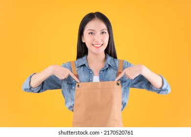 Pretty Asian Female Smile In Apron Freelancer Small Business And Startup Concept. Asian Woman Open Shop Pointing Finger With Apron Yellow Background.