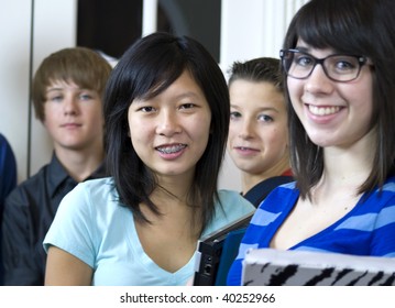 A pretty Asian girl with a group of her fellow schoolmates, stop and smile big for the camera.