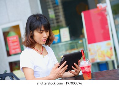 Pretty Asian Girl Reading Email On IPad In A Cafe