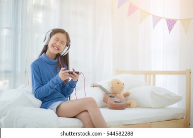 Pretty Asian Girl Using Headphone For Listen Music By Smartphone On The Bed In Her Decorated Bedroom